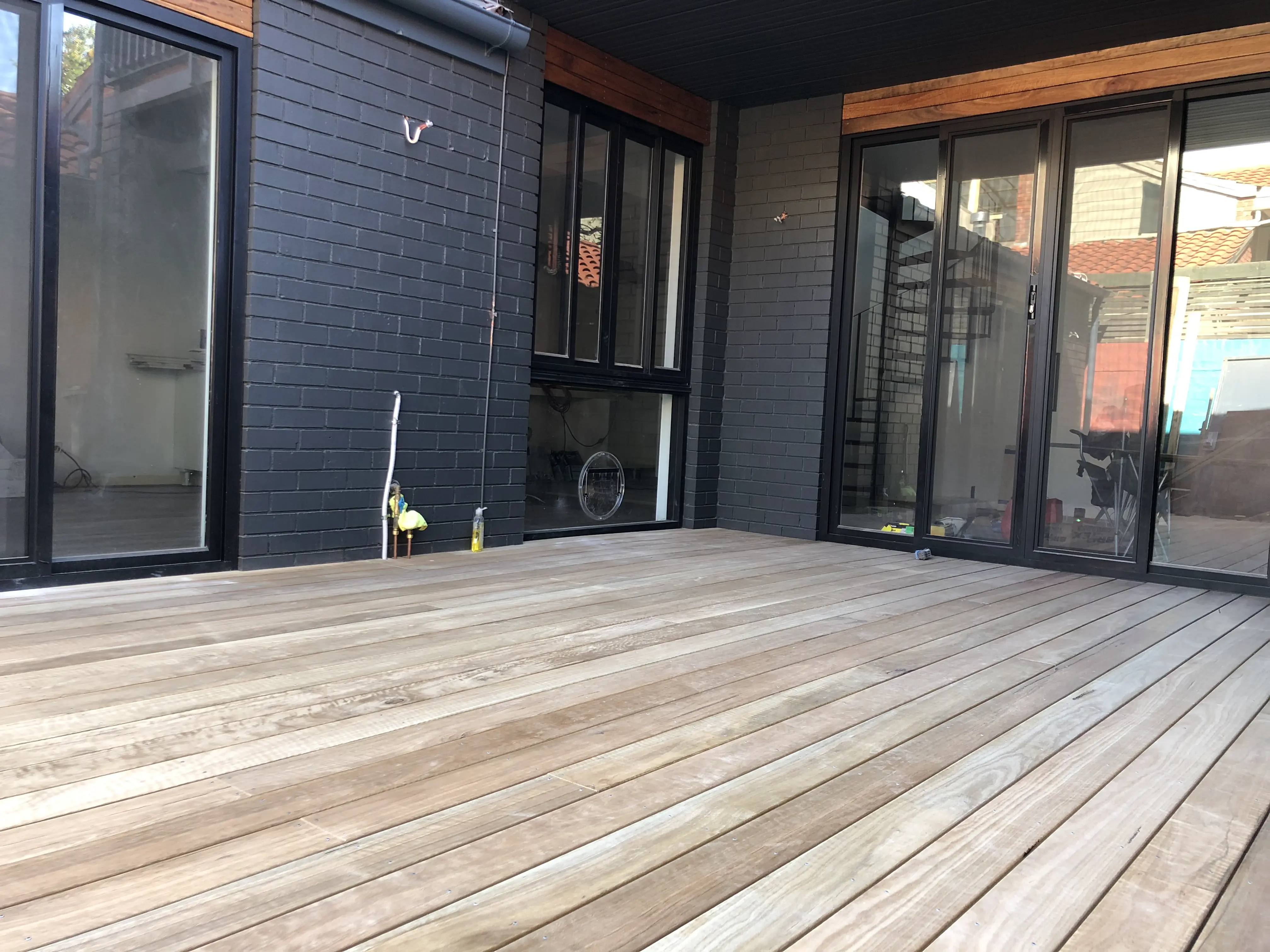 Timber deck against dark brick and black-framed doors
